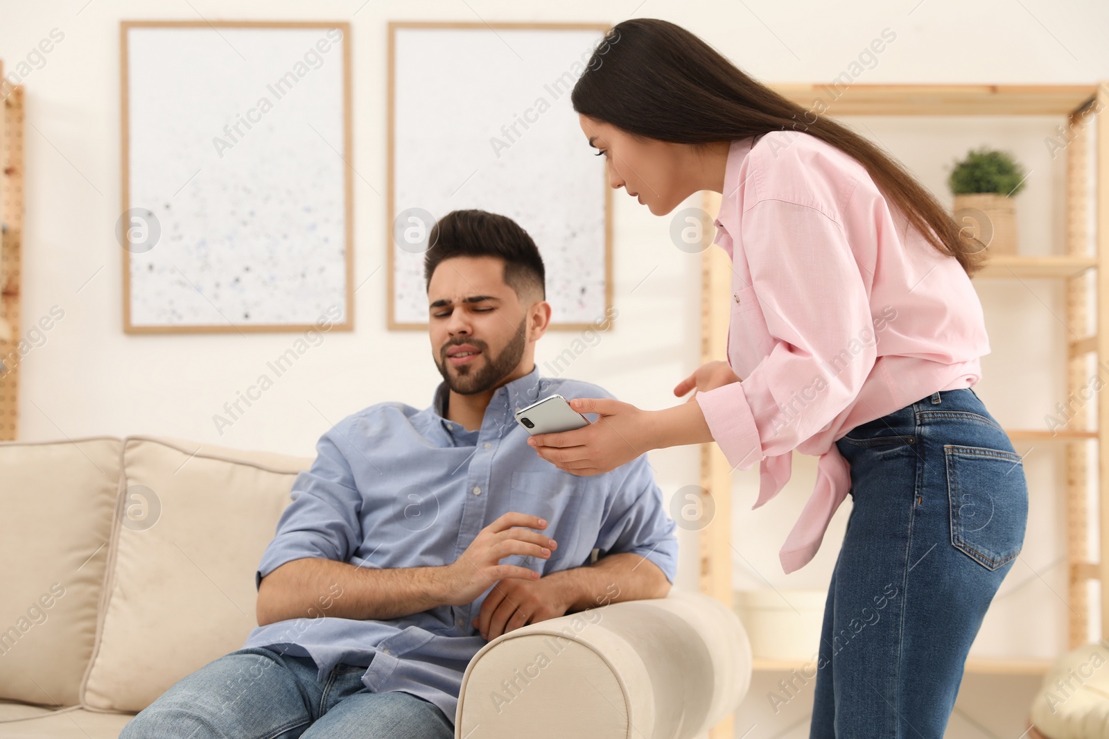 Photo of Young couple arguing about smartphone at home. Problems in relationship