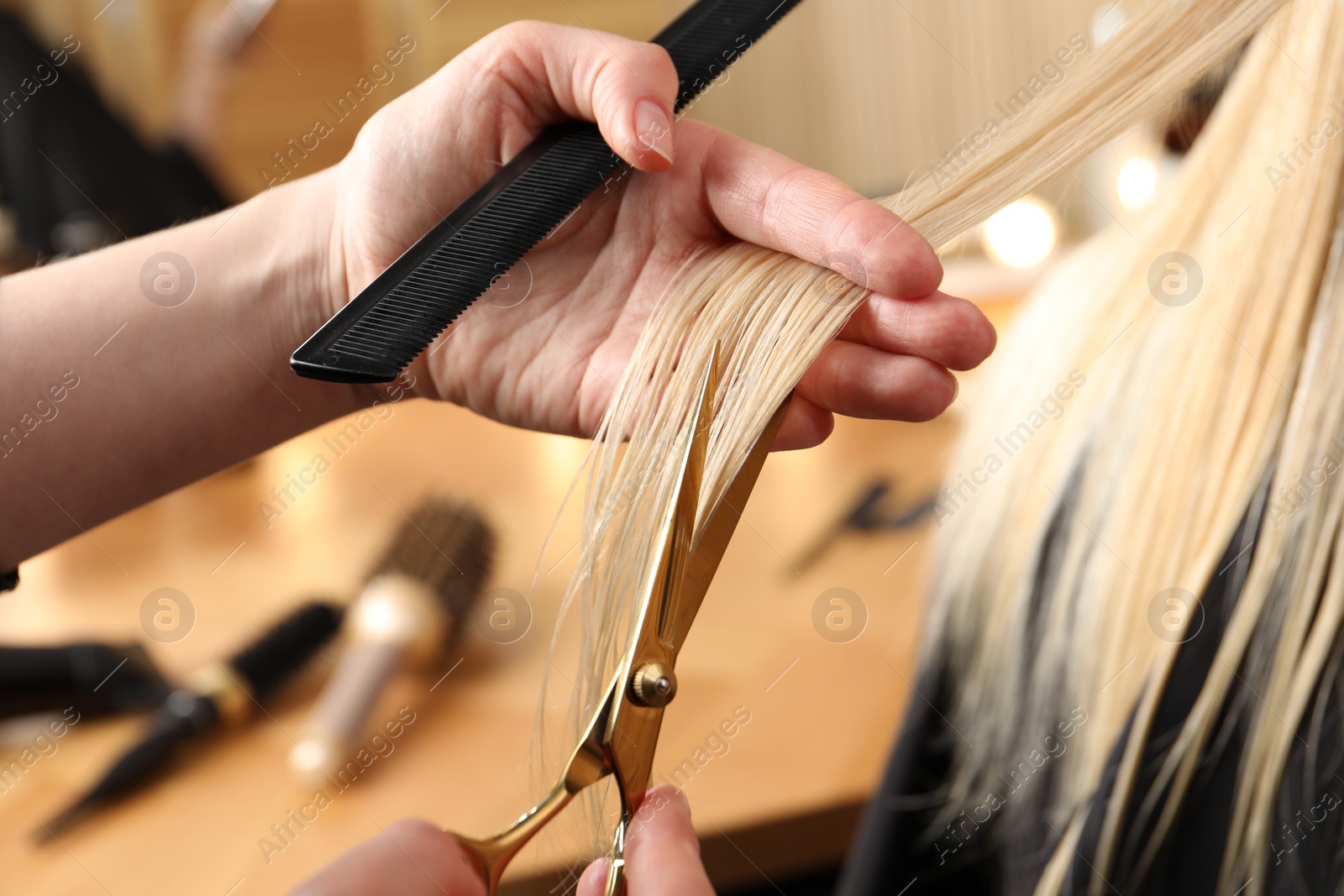 Photo of Hairdresser cutting client's hair with scissors in salon, closeup