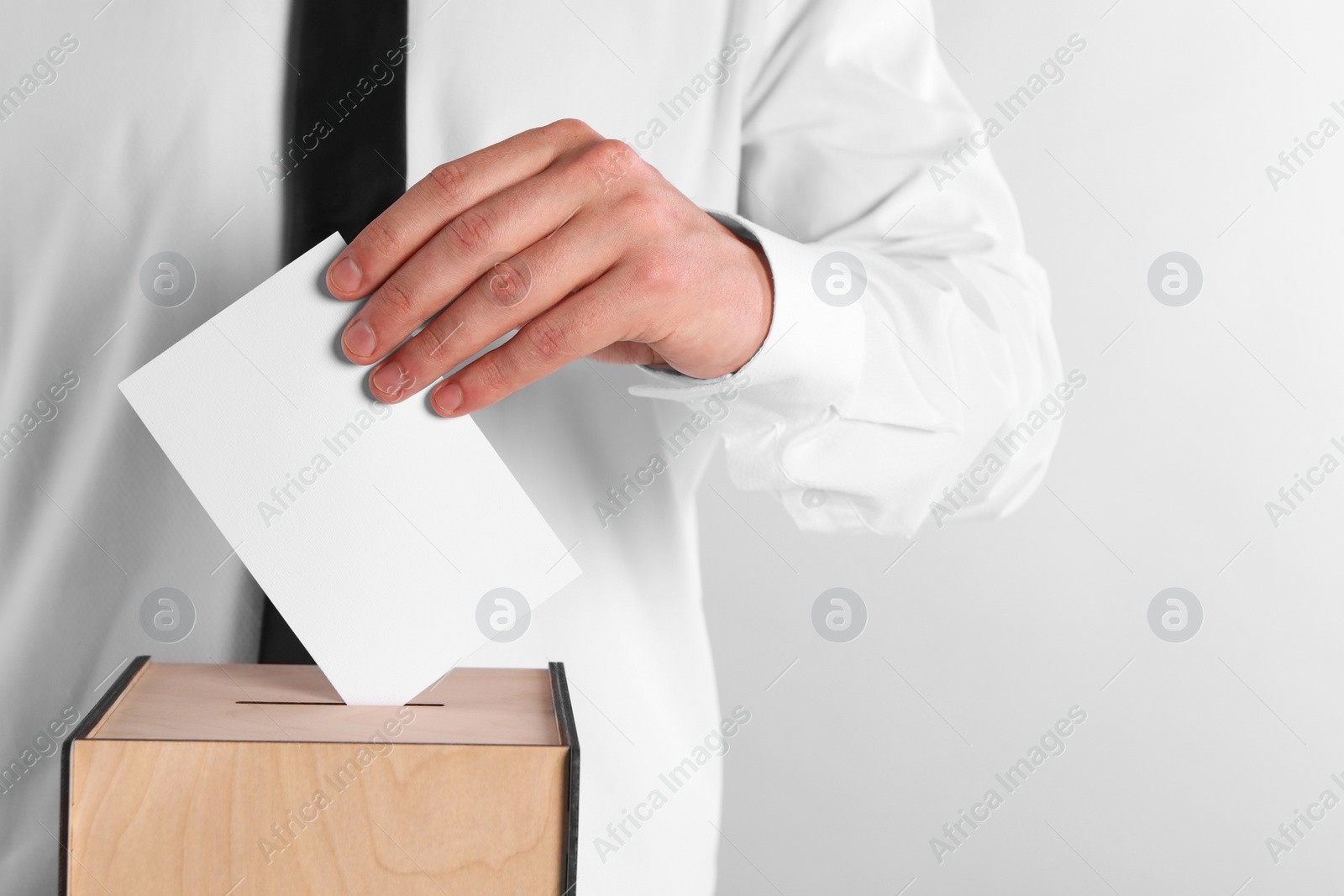 Photo of Man putting his vote into ballot box on light grey background, closeup