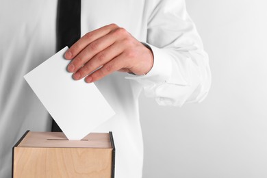 Man putting his vote into ballot box on light grey background, closeup