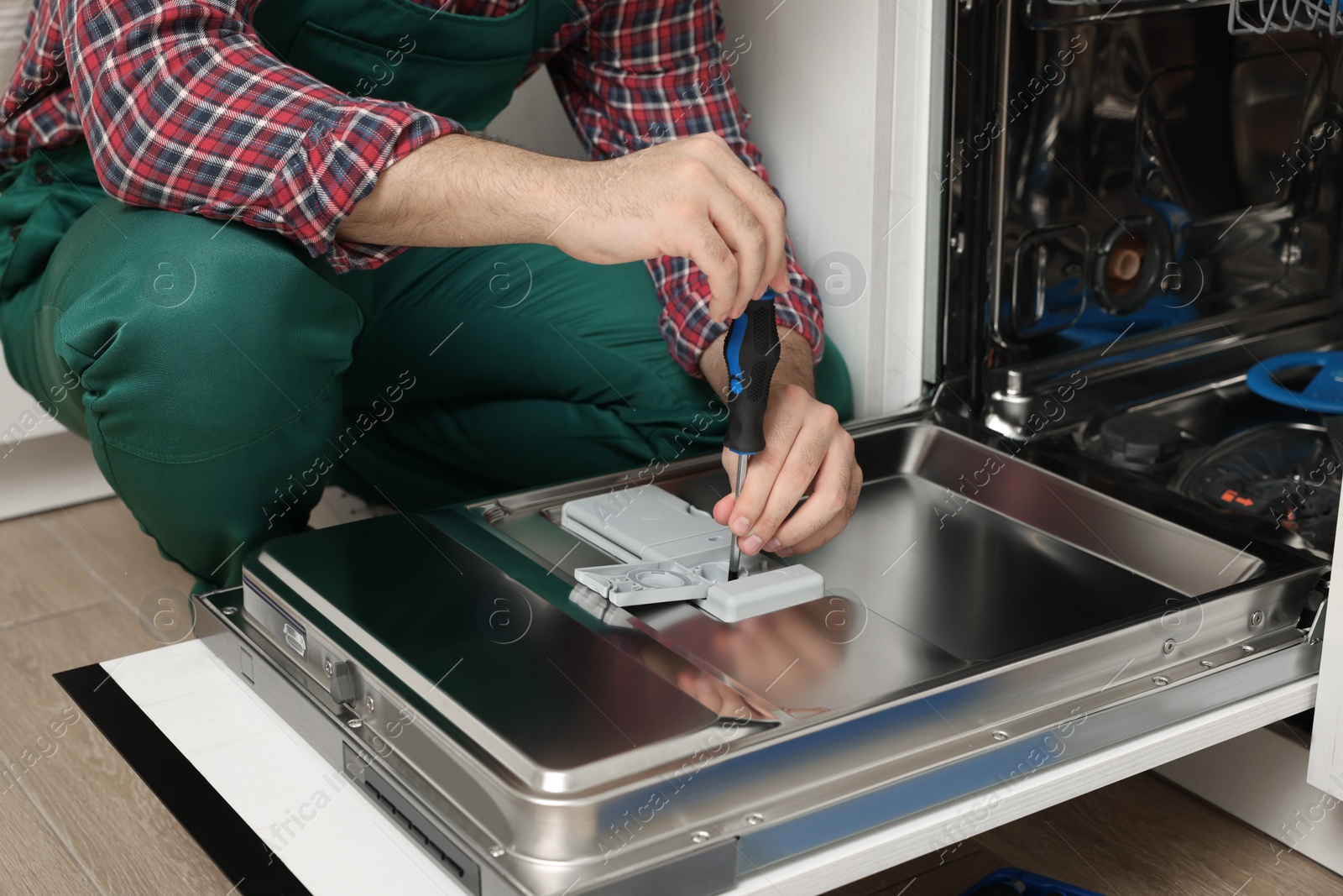 Photo of Serviceman repairing dishwasher with screwdriver indoors, closeup