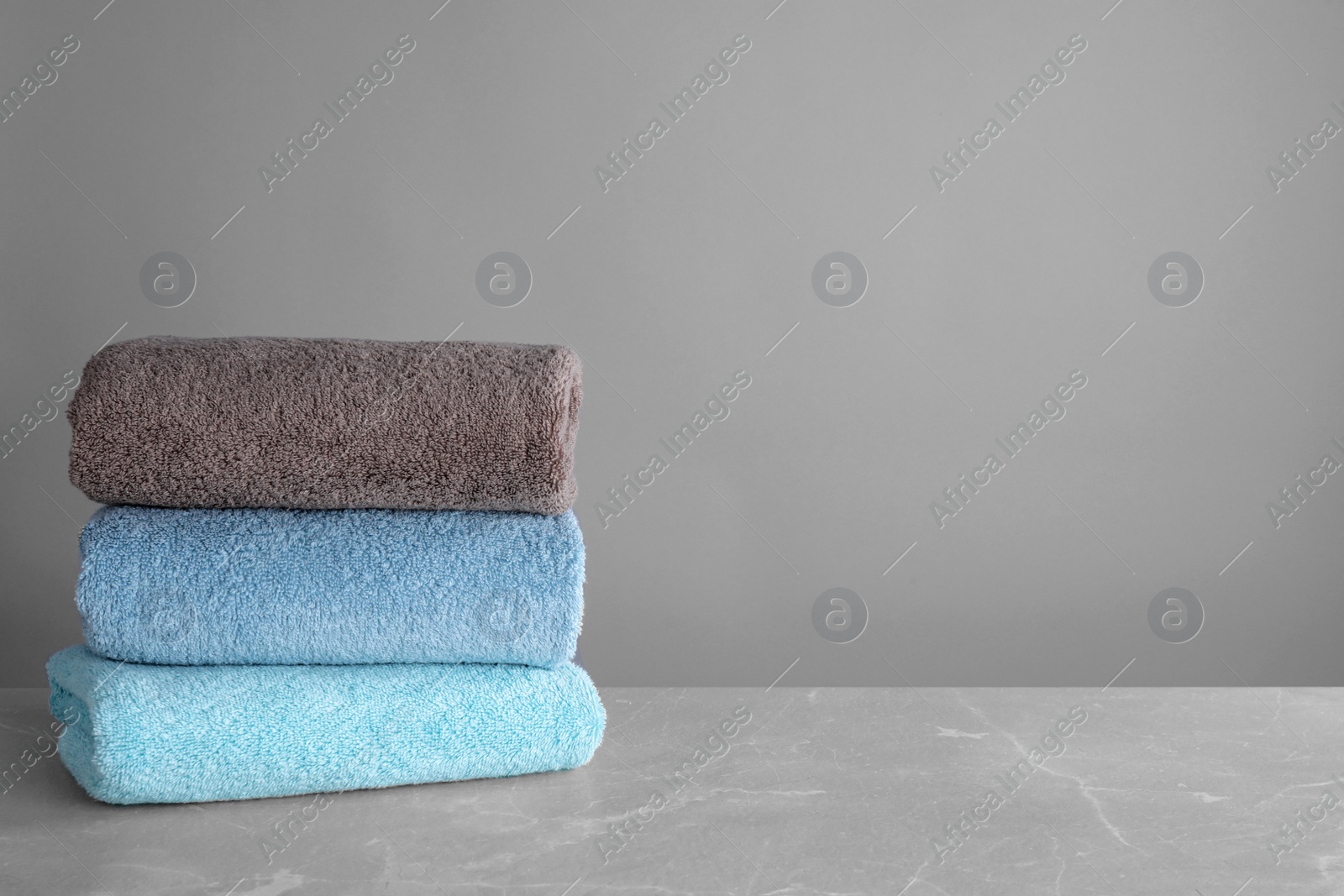 Photo of Stack of clean bath towels on grey table. Space for text