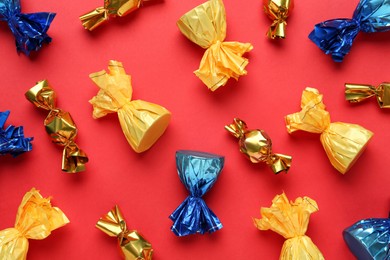 Photo of Many candies in colorful wrappers on red background, flat lay