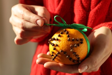 Woman holding pomander ball with green ribbon made of fresh tangerine and cloves on color background, closeup