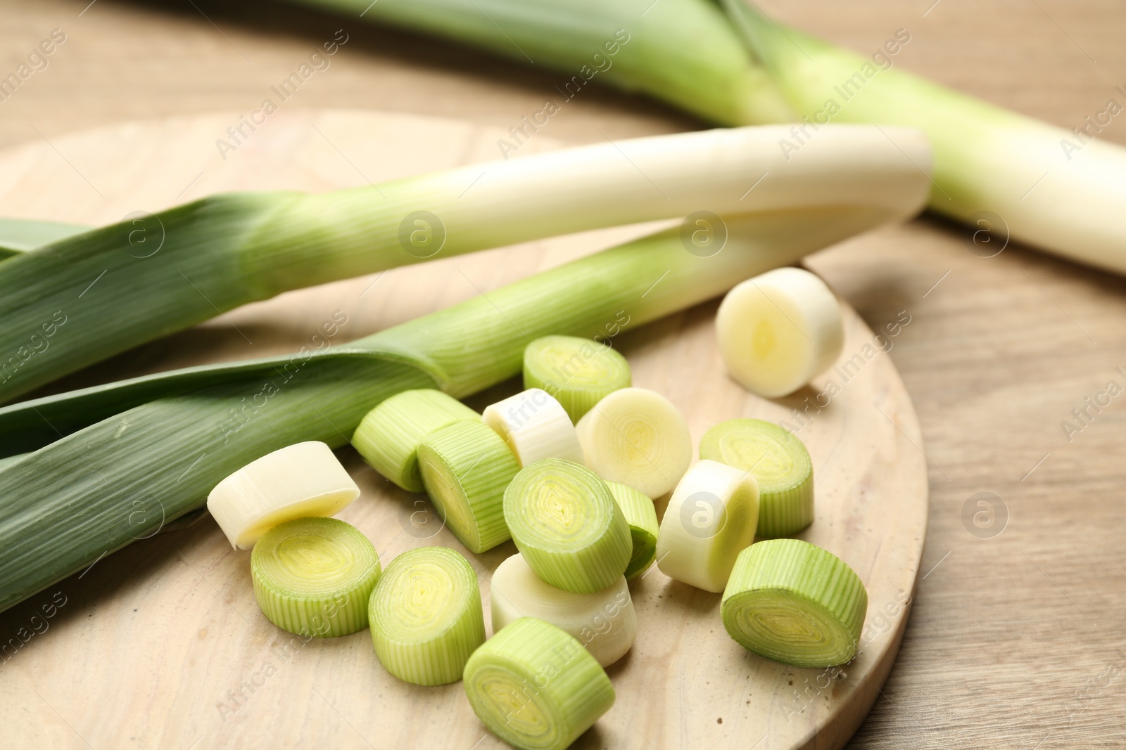 Photo of Whole and cut fresh leeks on wooden table, closeup
