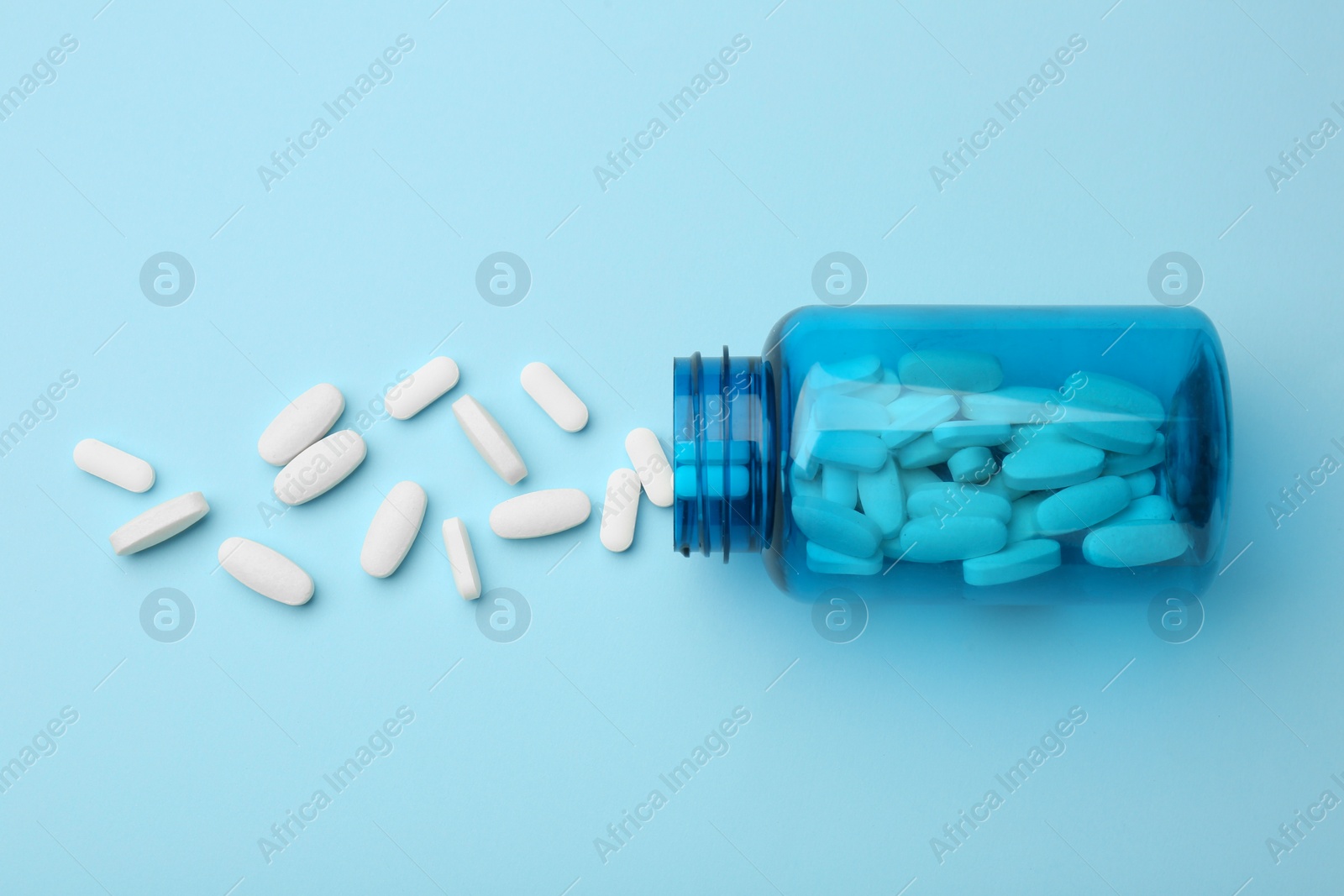 Photo of Vitamin pills and bottle on light blue background, top view