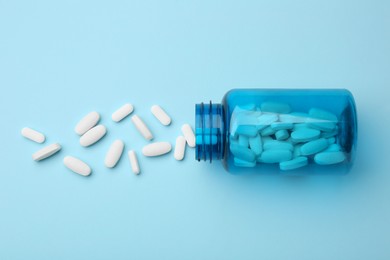 Photo of Vitamin pills and bottle on light blue background, top view