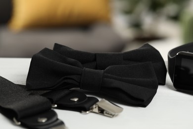 Photo of Stylish black bow ties, suspenders and smartwatch on white wooden table, closeup