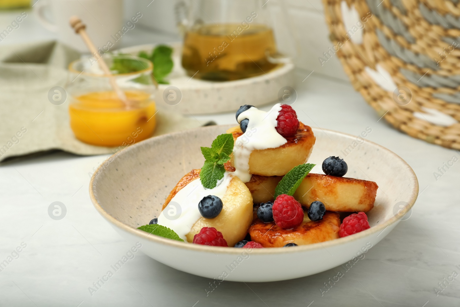 Photo of Delicious cottage cheese pancakes with fresh raspberries, sour cream and mint on white countertop