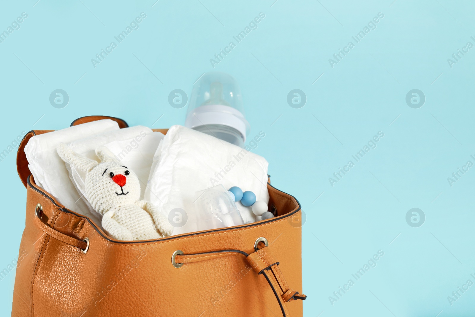 Photo of Mother's bag with baby's stuff on light blue background, closeup. Space for text