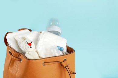 Photo of Mother's bag with baby's stuff on light blue background, closeup. Space for text