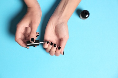 Woman applying nail polish on color background, top view with space for text