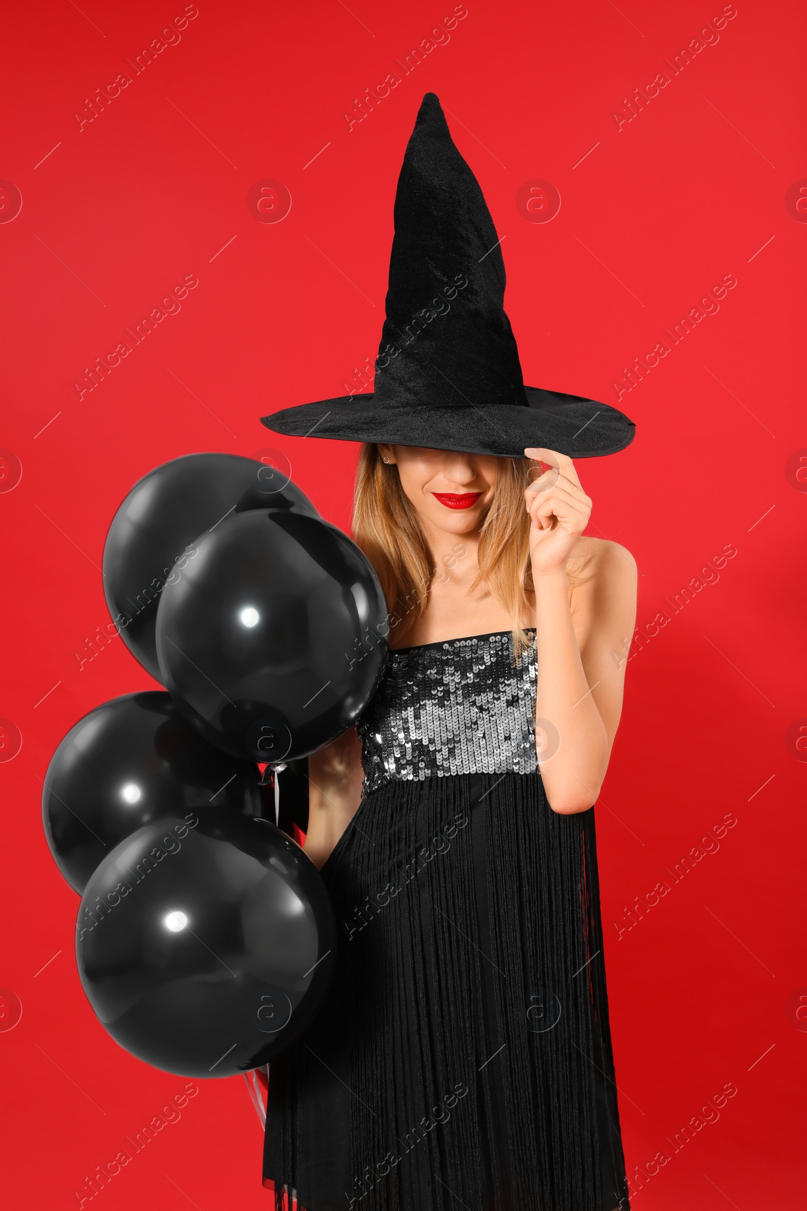 Photo of Beautiful woman wearing witch costume with balloons for Halloween party on red background