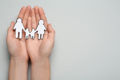 Photo of Woman holding paper family cutout on light grey background, top view. Space for text