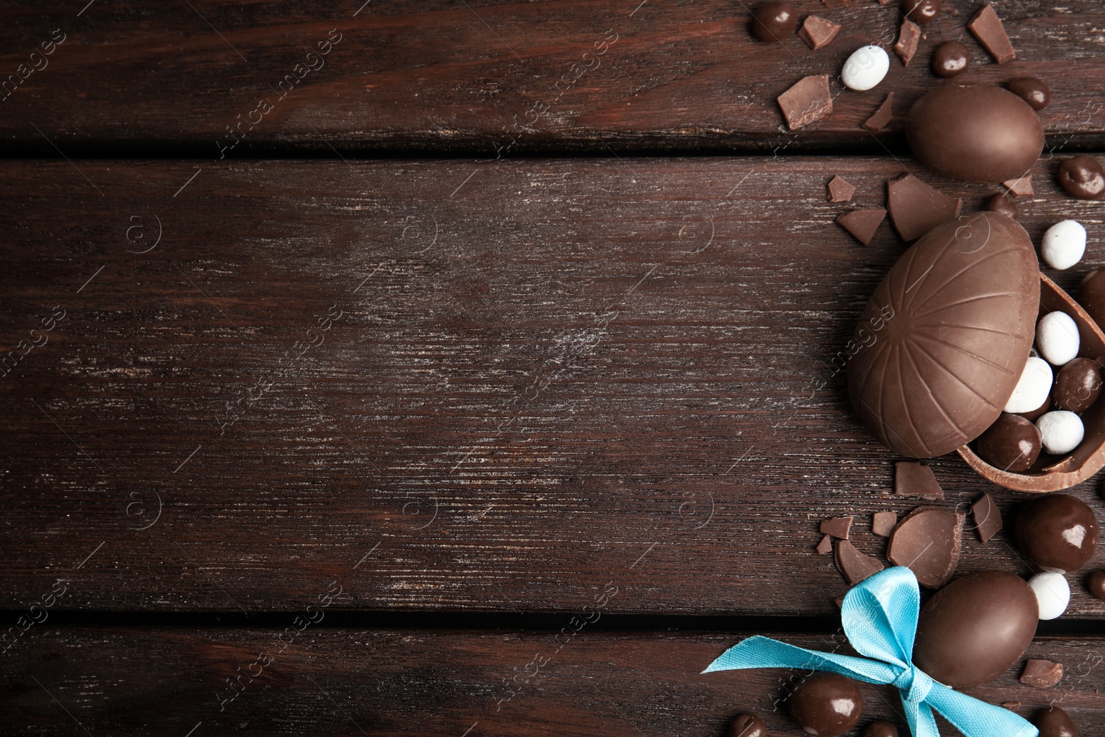 Photo of Flat lay composition with delicious chocolate Easter eggs and candies on wooden table. Space for text