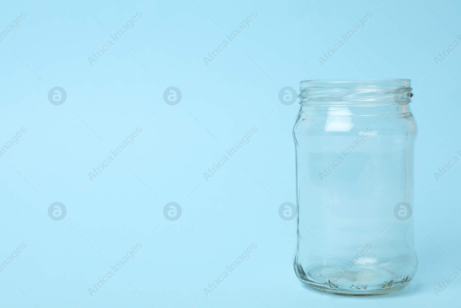 Photo of Open empty glass jar on light blue background, space for text