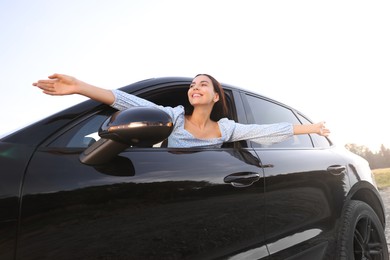 Photo of Enjoying trip. Happy woman leaning out of car window outdoors, low angle view