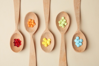 Wooden spoons with different pills on color background, top view