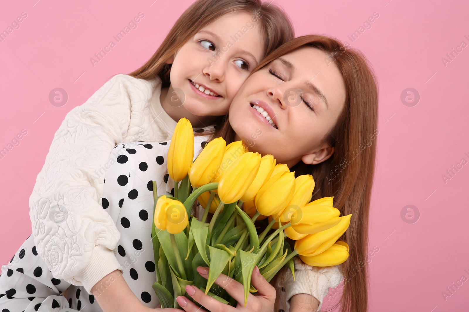 Photo of Mother and her cute daughter with bouquet of yellow tulips on pink background