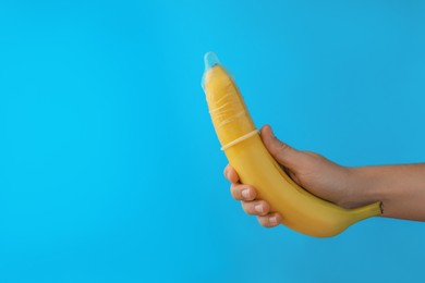 Photo of Woman holding banana in condom on light blue background, closeup and space for text. Safe sex concept