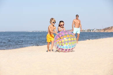 Little children with inflatable ball and their father on sandy beach near sea. Summer holidays with family
