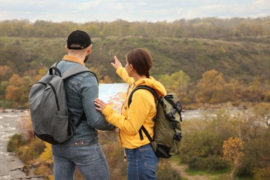 Couple of travelers with backpacks and map enjoying beautiful view near mountain river, back view. Autumn vacation