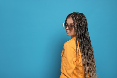 Beautiful woman with long african braids and sunglasses on blue background, space for text