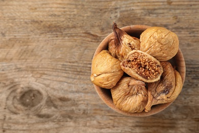 Photo of Bowl of dried figs on wooden table, top view. Space for text