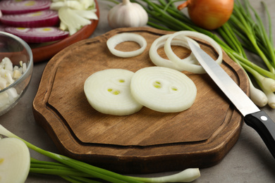 Photo of Fresh onion, knife and wooden board on grey table, closeup