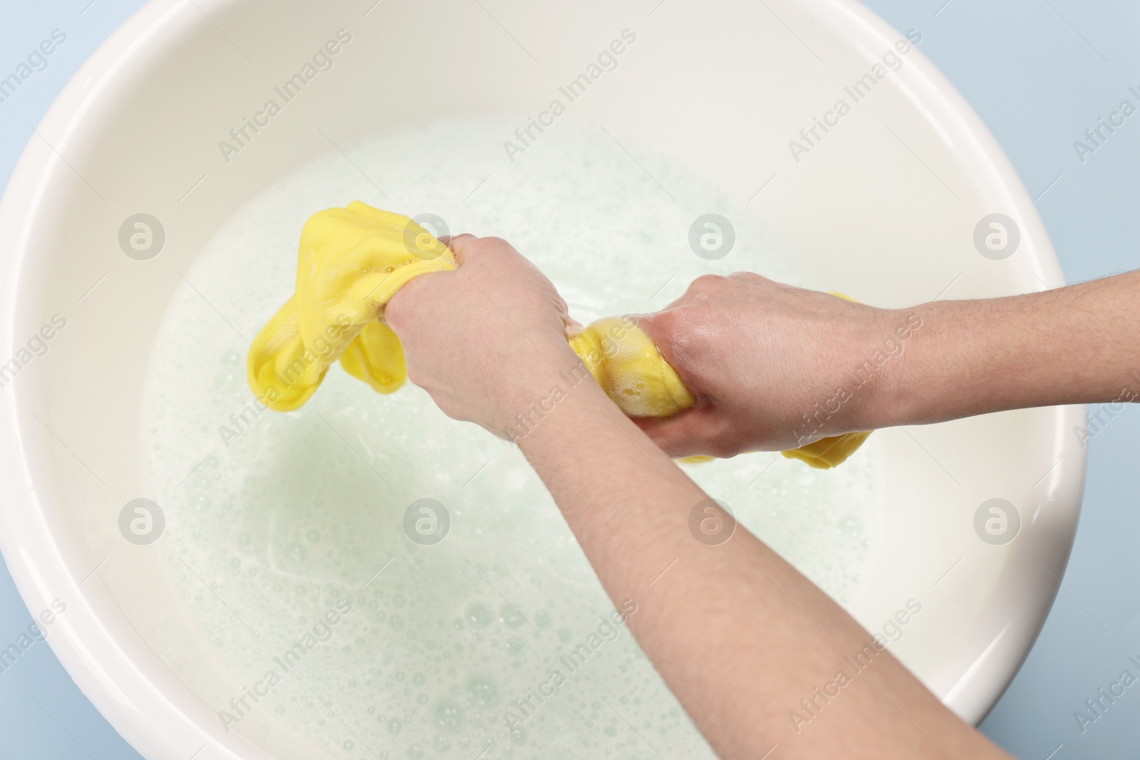 Photo of Woman washing baby clothes in basin on light blue background, closeup