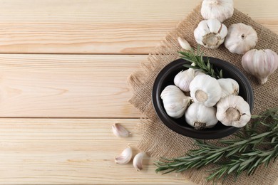 Fresh raw garlic and rosemary on wooden table, flat lay. Space for text