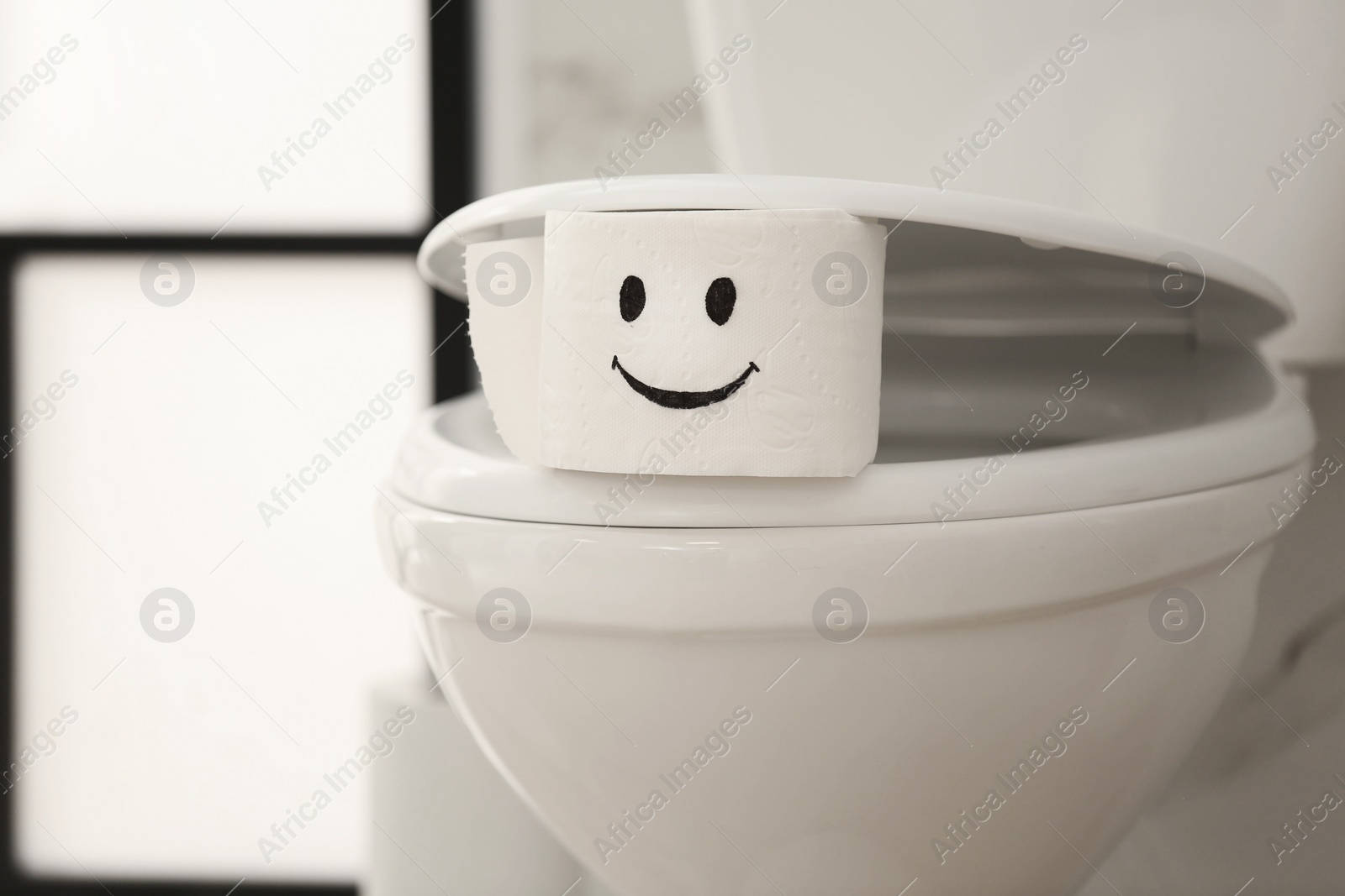 Photo of Roll of paper with funny face on toilet bowl in bathroom