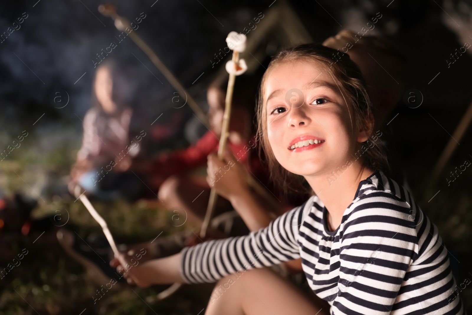 Photo of Adorable little girl near bonfire at night. Summer camp