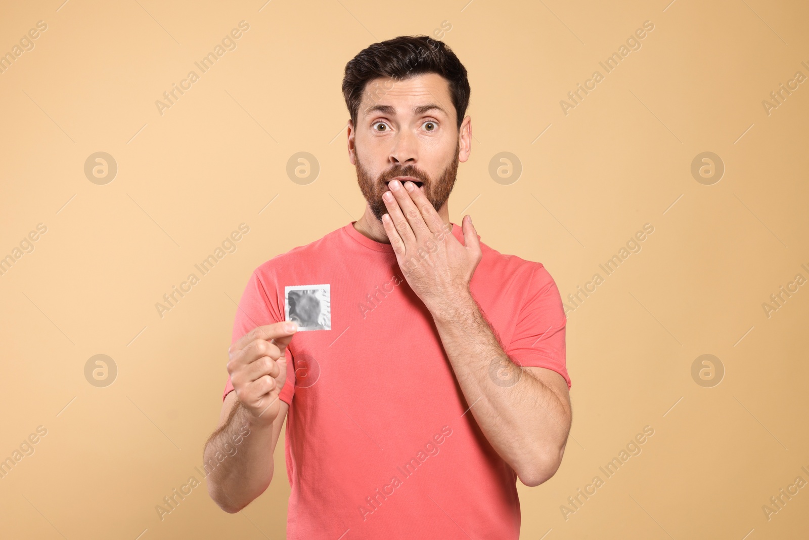 Photo of Emotional man holding condom on beige background. Safe sex