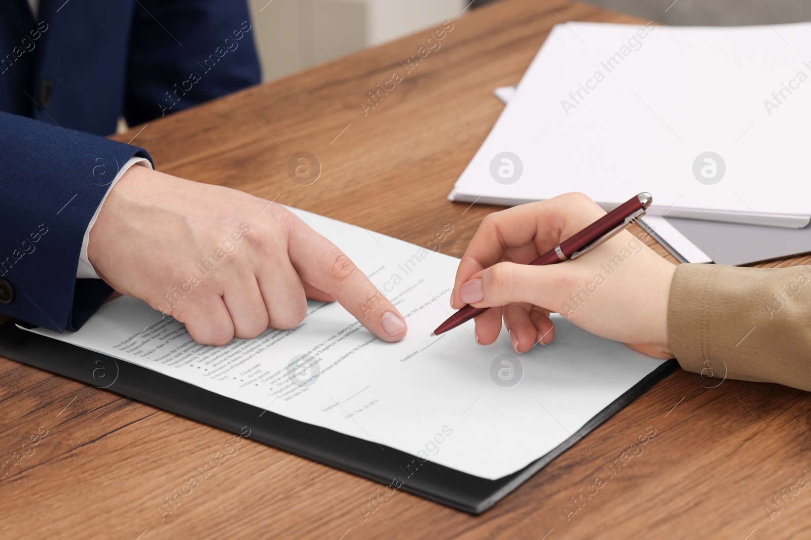 Photo of Man pointing at document and woman putting signature at wooden table, closeup