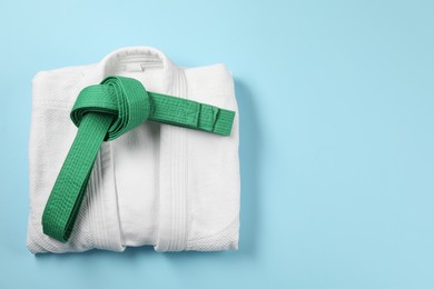 Photo of Green karate belt and white kimono on light blue background, top view. Space for text