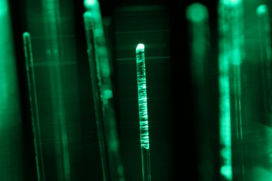 Optical fiber strands transmitting green light on black background, macro view