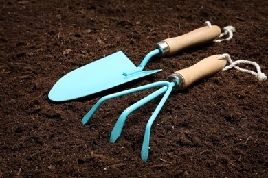 Photo of Metal gardening trowel and rake on fertile soil