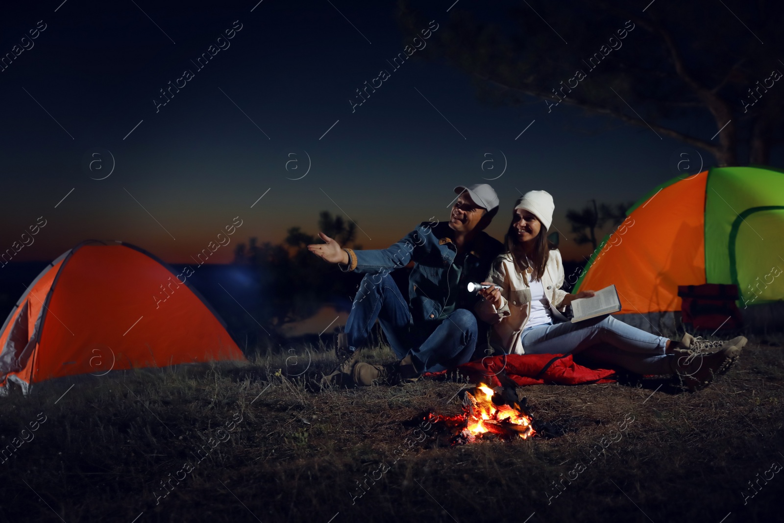 Photo of Couple with flashlight near bonfire at night. Camping season