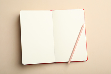 Photo of Stylish open notebook and pencil on beige background, top view