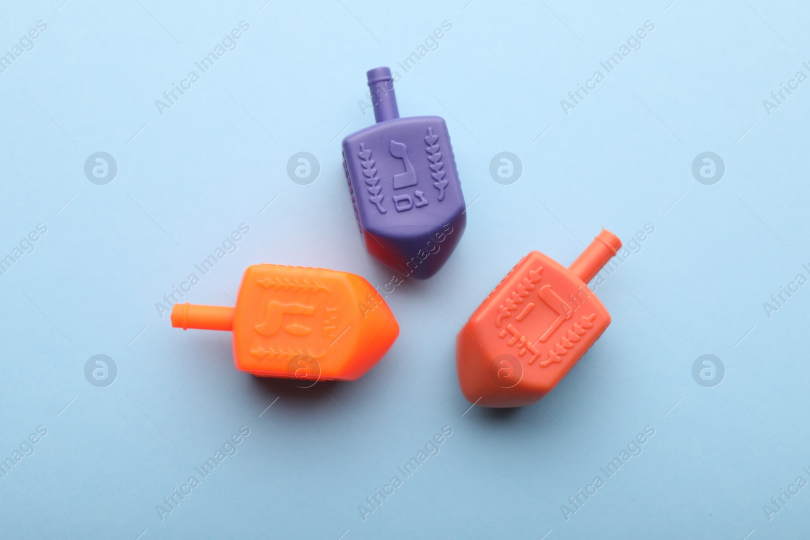 Photo of Colorful dreidels on light blue background, flat lay. Traditional Hanukkah game
