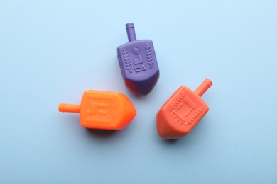 Photo of Colorful dreidels on light blue background, flat lay. Traditional Hanukkah game