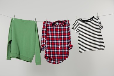 Photo of Different shirts drying on laundry line against light background