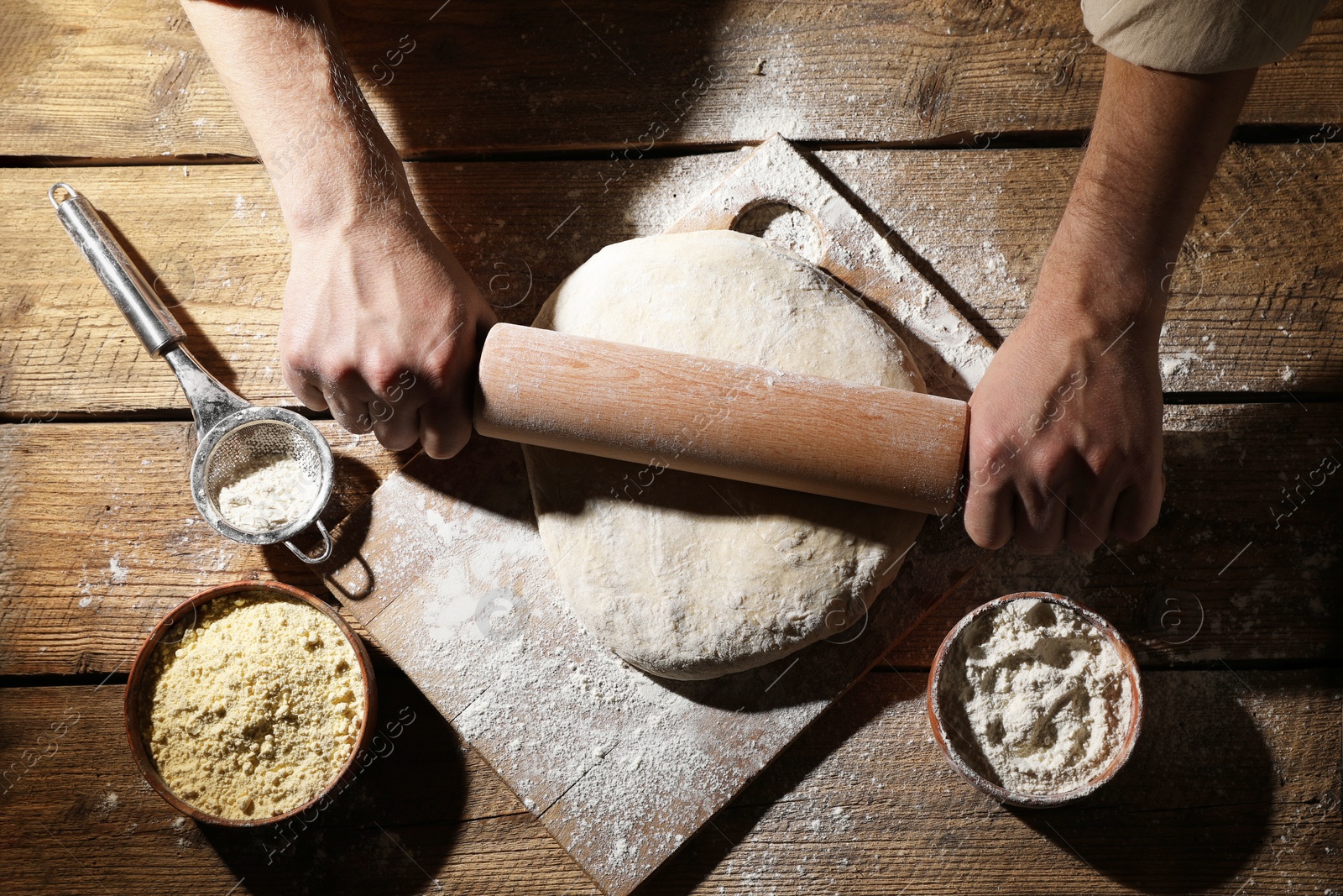 Photo of Man rolling raw dough at wooden table, closeup