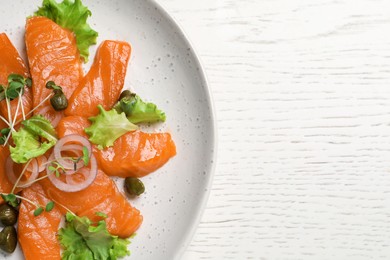 Salmon carpaccio with capers, lettuce, microgreens and onion on white wooden table, top view. Space for text