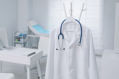 Photo of White doctor's gown and stethoscope hanging on rack in clinic