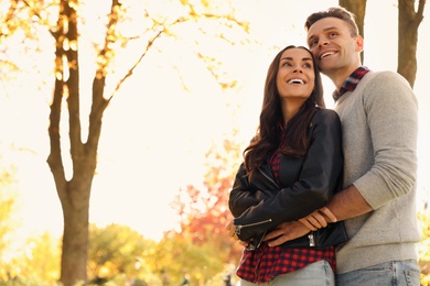 Photo of Happy couple in sunny park, low angle view. Autumn walk