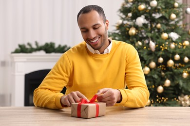 Happy man opening Christmas gift at wooden table in room