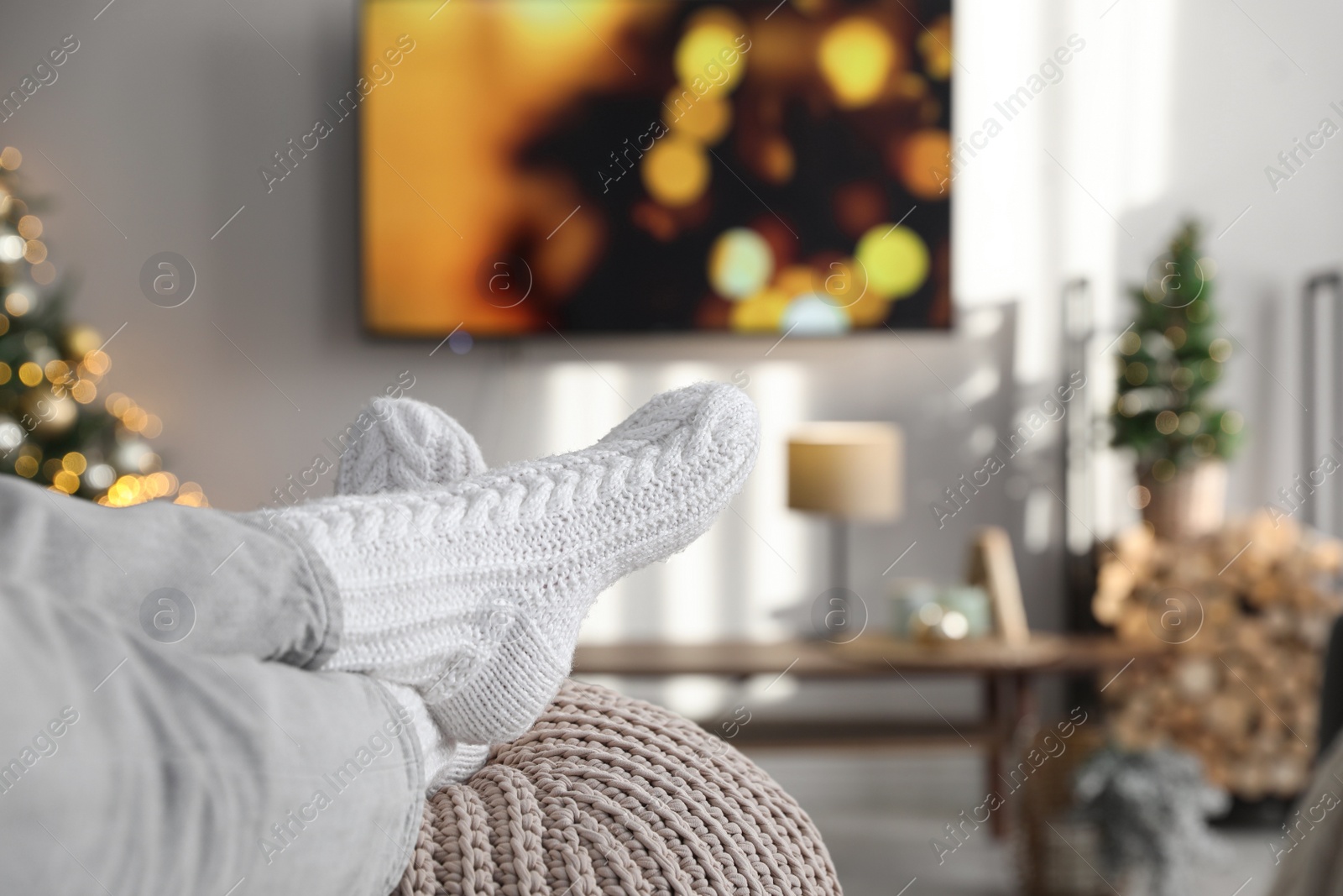 Photo of Woman wearing knitted socks in room decorated for Christmas, closeup