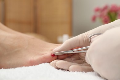 Pedicurist cutting client`s toenails with scissors in beauty salon, closeup